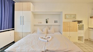 A hotel room with a bed, a small shelf with decorative items, a microwave, and a cabinet. - Windrose Appartement 1 - Haus Windrose (Scharbeutz)