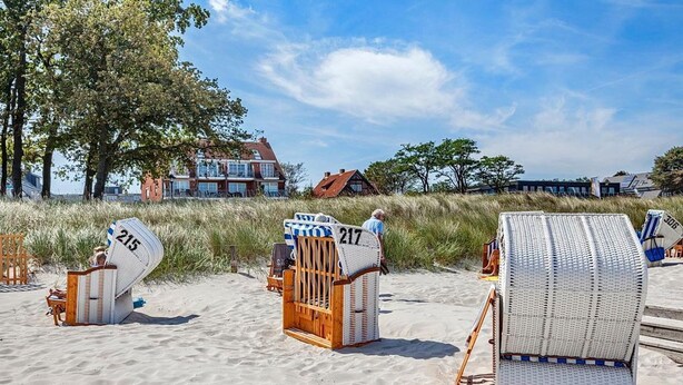 Beach chairs with numbers 215 and 217, a wooden bench, and a beach setting with buildings in the background. - Windrose Appartement 1 - Haus Windrose (Scharbeutz)