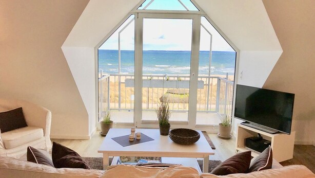 Ein modernes Wohnzimmer mit großem Fenster mit Meerblick, einem Flachbildfernseher und einer gemütlichen Sitzecke.
