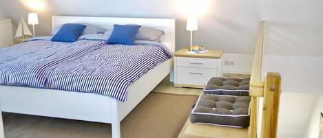 A neatly arranged bedroom with a bed, bedside tables, a nightstand, and a small stool.