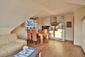 Una sala de estar acogedora con un sofá y un comedor con una mesa de madera y sillas. Se ve una cocina con microondas y refrigerador al fondo.