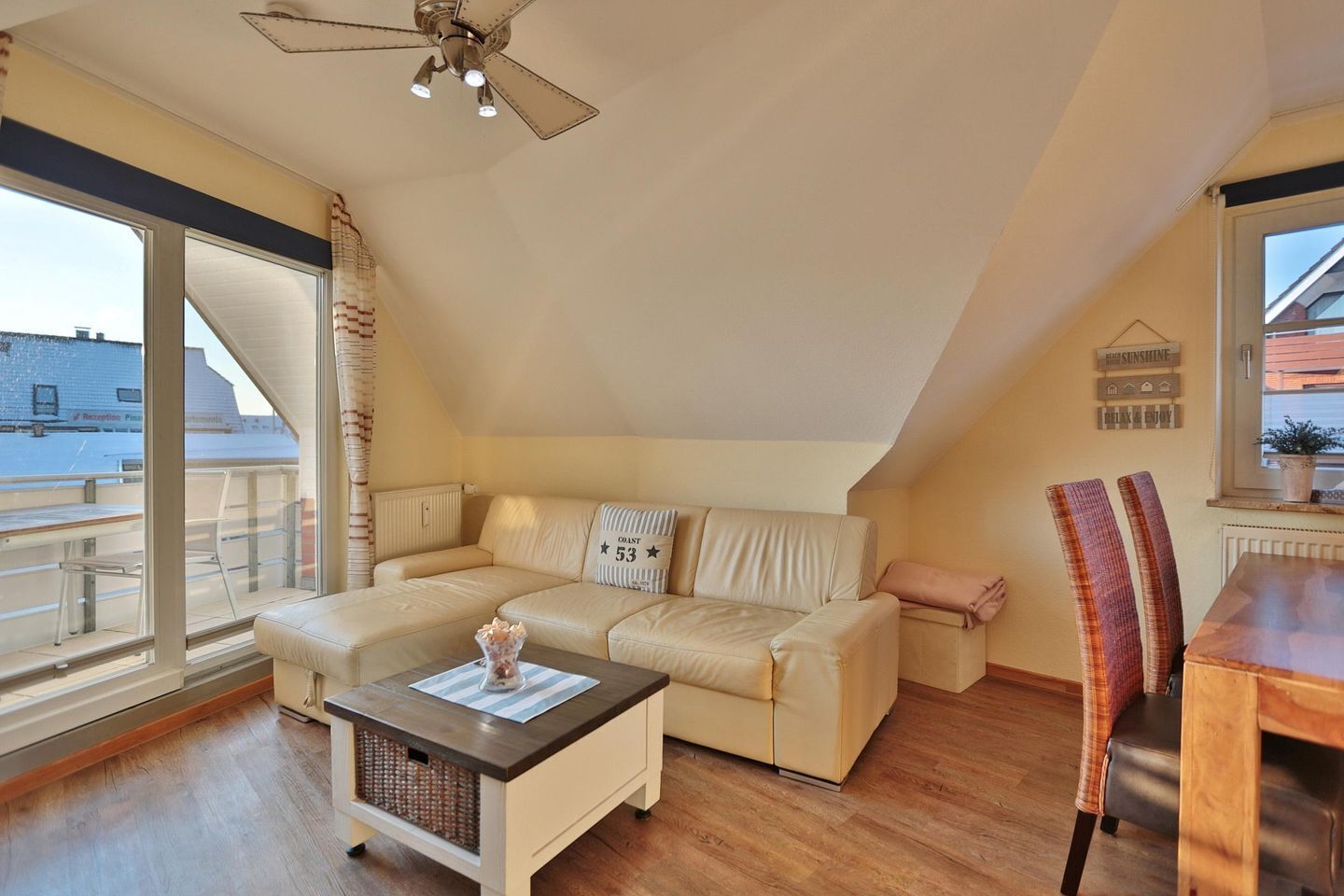 Um apartamento loft acolhedor com uma janela grande, ventoinha no teto, sofá, mesa de jantar e uma cadeira.