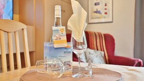 Ein Hotelzimmer mit einem Holzstuhl, einem Tisch mit einer Weinflasche, einem Glas und einer Serviette. An der Wand hängt ein gerahmtes Bild und im Hintergrund steht ein rotes Sofa.