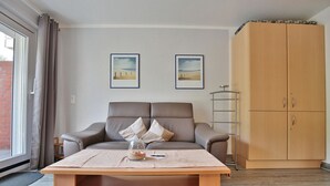 Ein Wohnzimmer mit einer Couch, einem Couchtisch und einem Schrank. An der Wand hängen zwei gerahmte Bilder.