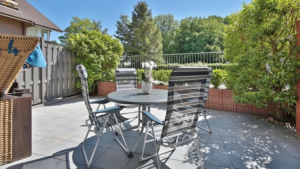 Eine Terrasse im Freien mit einem runden Tisch und zwei Stühlen, umgeben von einer Ziegelmauer und viel Grün.