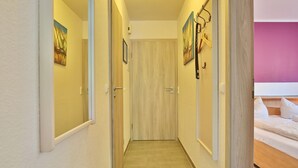 Ein Hotelgang mit Holztüren, einem Bett mit weißer Bettwäsche und einer rosafarbenen Wand.