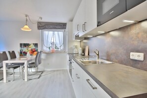 A modern kitchen with a stainless steel sink, white cabinets, and a dining area with a table and chairs.