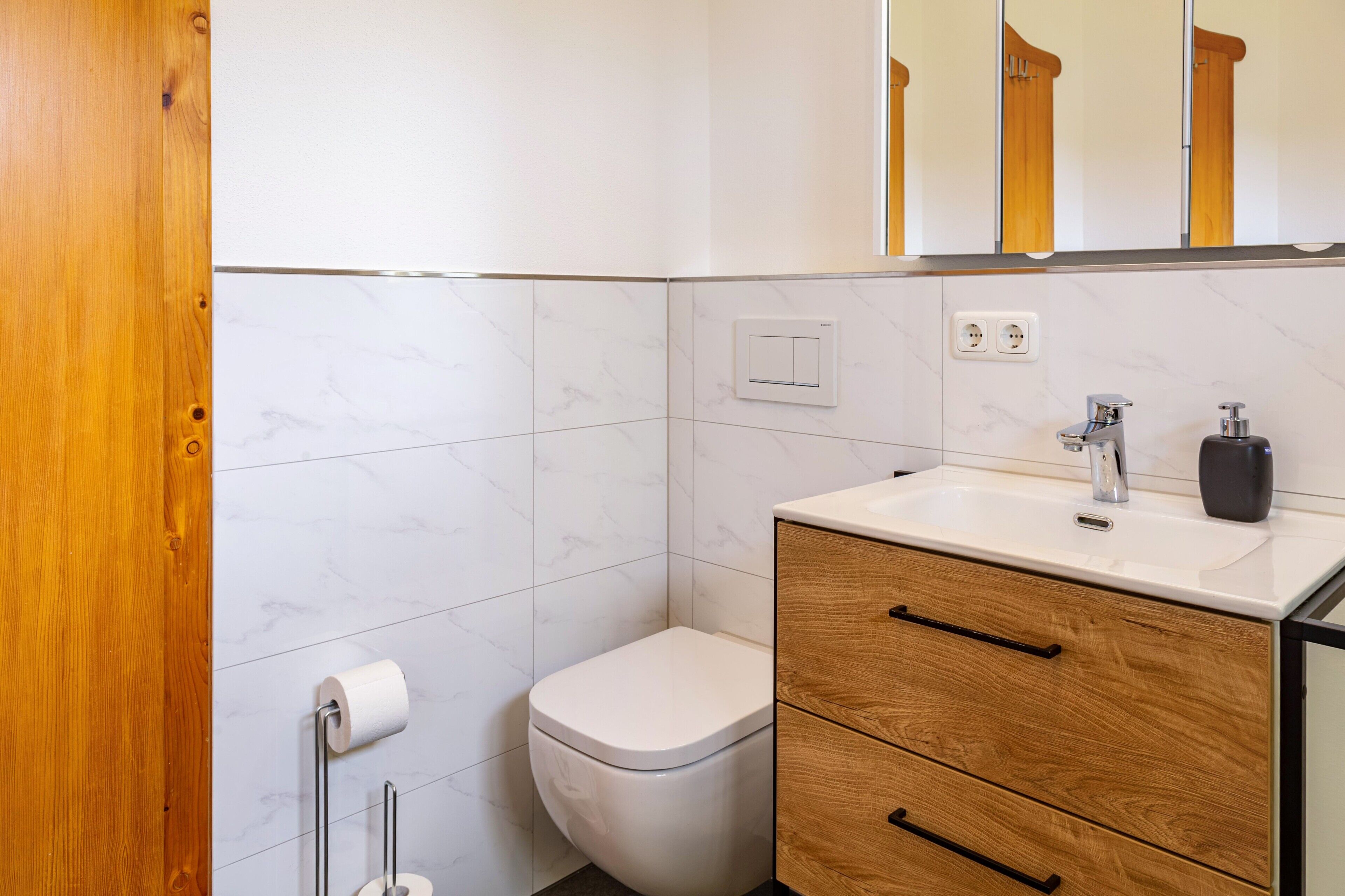 Ein Badezimmer mit Toilette, Waschbecken, Holzschrank und Spiegel.