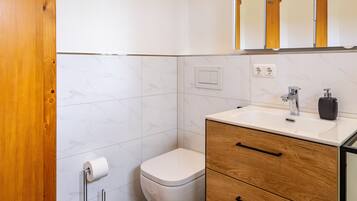 Ein Badezimmer mit Toilette, Waschbecken, Holzschrank und Spiegel.