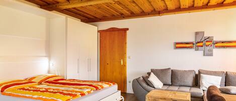 Un dormitorio con cama, techo de madera, sofá, mesa de centro y una puerta.
