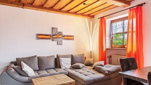 A modern living room with a sectional sofa, a wooden coffee table, and a window with curtains. - Comfort apartment with pool, sauna and Wi-Fi (Hauzenberg)