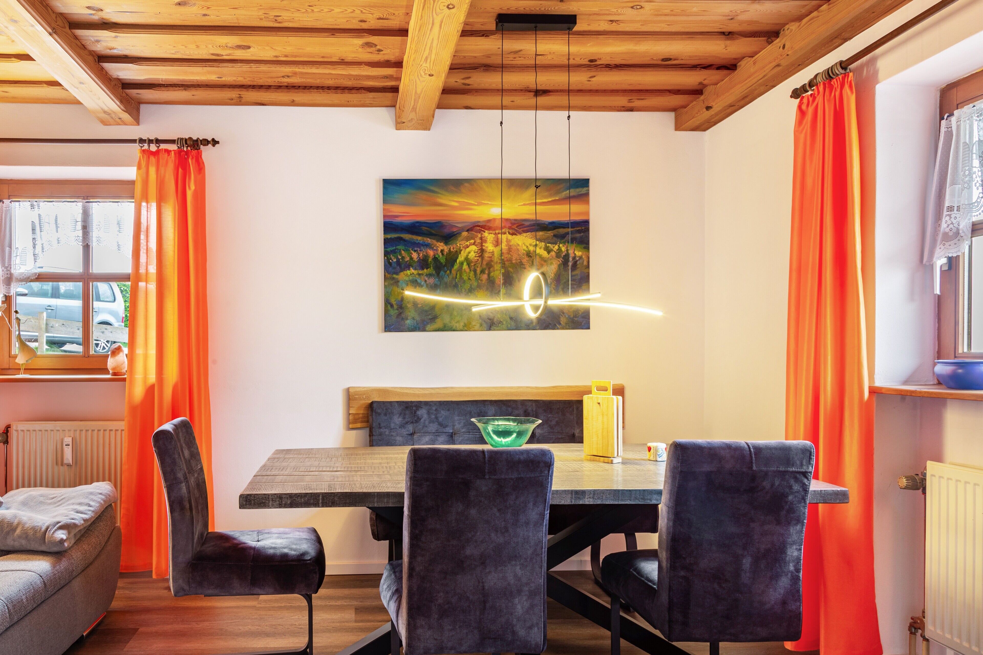 A dining area with a wooden table, black chairs, and a painting of a sunset.