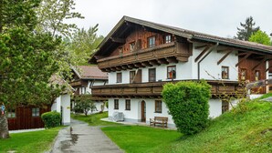 A traditional chalet with a sloped roof, wooden balconies, and a paved driveway leading to a bench. - Comfort apartment with pool, sauna and Wi-Fi (Hauzenberg)