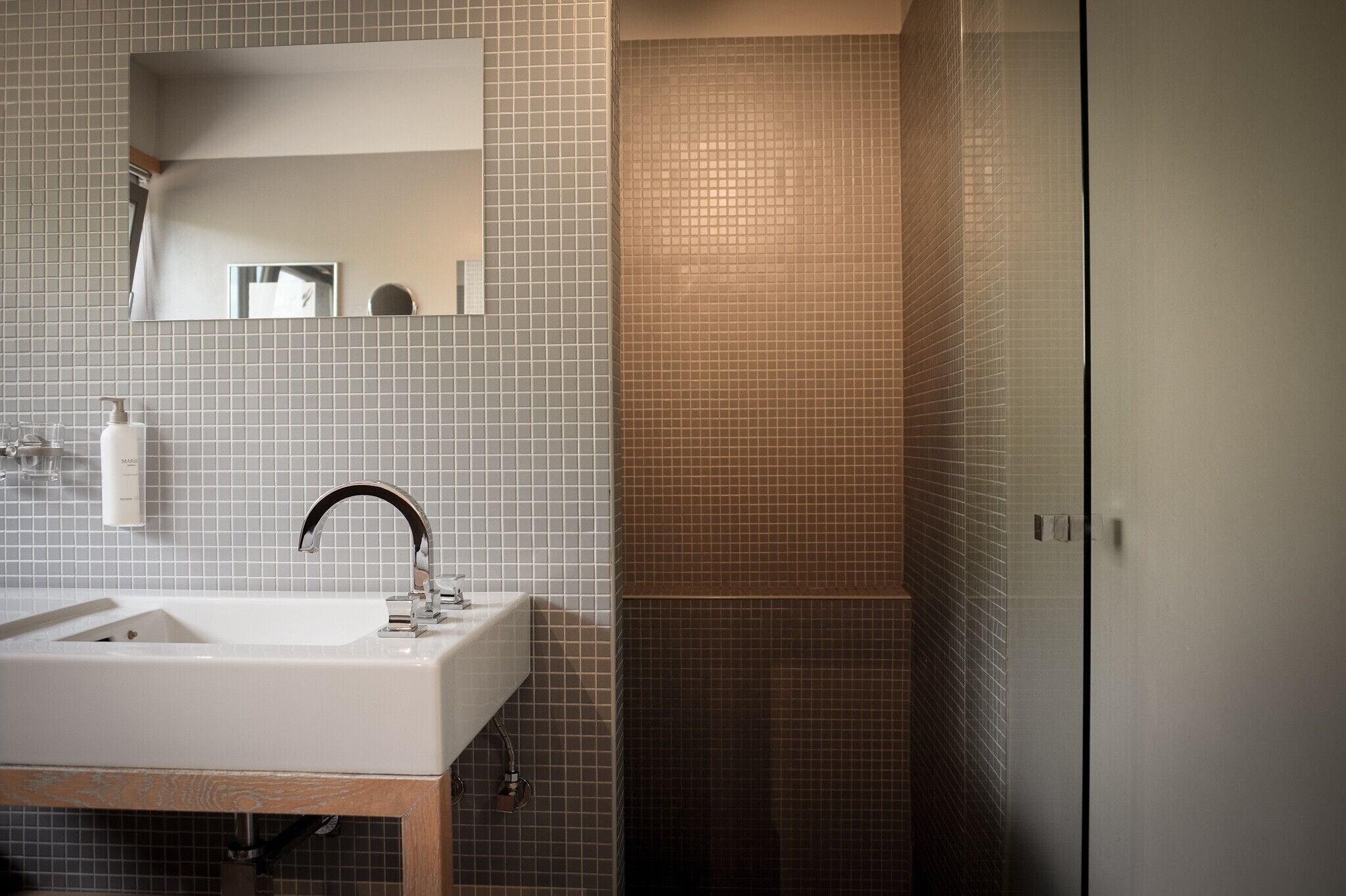 A bathroom with a sink, mirror, and shower area.