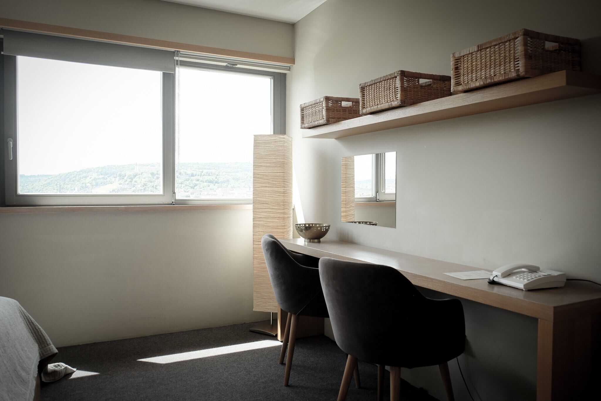Quarto de hotel moderno com escrivaninha, duas cadeiras, telefone e janela com vista.