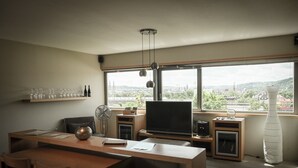 Un espace de vie moderne comprenant un coin repas, un téléviseur à écran plat et une grande fenêtre donnant sur la ville.