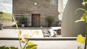 Un bâtiment moderne avec une façade en béton, une porte en bois et un espace extérieur aménagé avec des chaises et des tables.