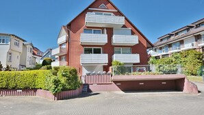 Un edificio residencial de varios pisos con balcones, un camino pavimentado y un jardín bien cuidado.