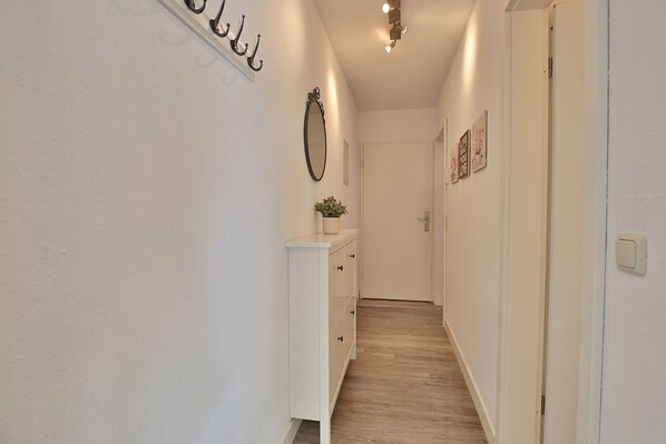 Un couloir étroit avec une commode blanche, un miroir et une plante en pot.