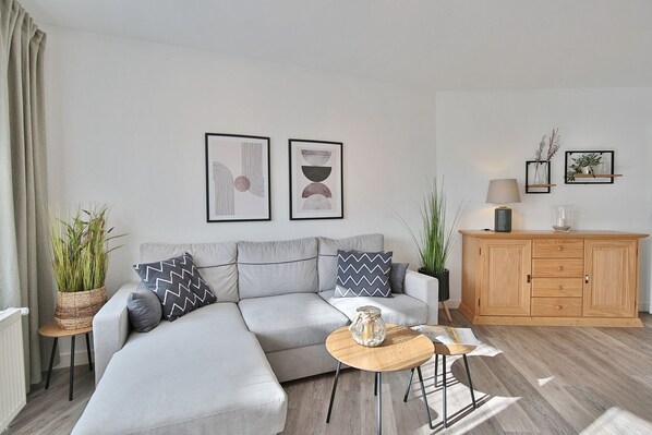 Un salon moderne avec un canapé d’angle gris, un buffet en bois et deux œuvres d’art abstraites encadrées accrochées au mur.