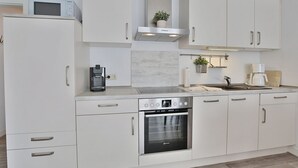 Una cocina moderna con armarios blancos, horno empotrado, cafetera y microondas.