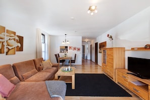 Un salon moderne comprenant un canapé, un téléviseur, des meubles en bois et un coin repas avec des chaises et une table.