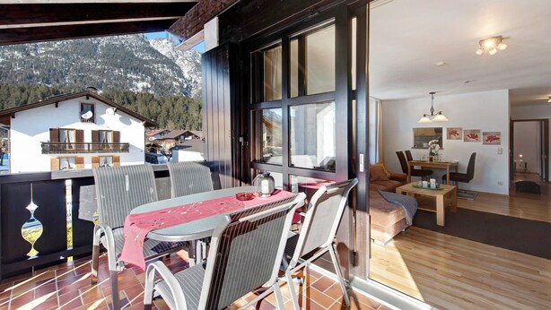 Ein Essbereich mit Tisch und Stühlen, ein Balkon mit Bergblick und ein Wohnzimmer mit Sofa und Tisch.