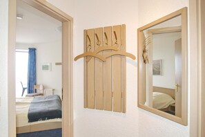 A hotel room with a bed, a wooden coat rack, and a mirror.