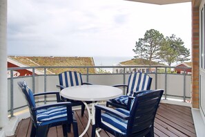A covered outdoor seating area with a round table and striped chairs, overlooking a residential area with houses and a tree.