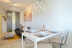 Un espace repas moderne avec une table blanche, des chaises transparentes et une bouteille d’eau.