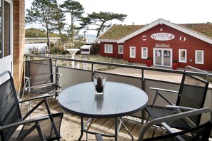 A balcony with a round table and chairs, overlooking a red building with a sign that reads 'GOSCH' and 'Kongens Pilsener.' - Residenz Ostseestrand Appartement 10 - Residenz Ostseestrand (Scharbeutz)
