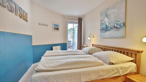 A hotel room with a large bed, a wooden headboard, a painting of sailboats, a window with a view, and a blue and white wall design.