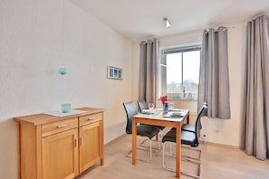 Un comedor con una mesa de madera, sillas negras, un mueble de madera y una ventana con cortinas.