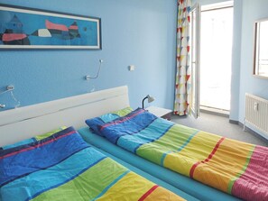 Ein Schlafzimmer mit zwei Betten, einem Nachttisch, einer Lampe, einem Fenster mit Vorhängen und einem Bild an der Wand.