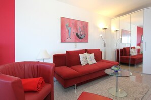 Una sala de estar moderna con un sofá rojo, una mesa de centro de vidrio y un cuadro en la pared.