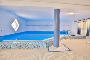 Ein Innenpool mit Fliesenboden und -wänden, einer zentralen Säule und einer kleinen Sitzecke mit einer Leiter.