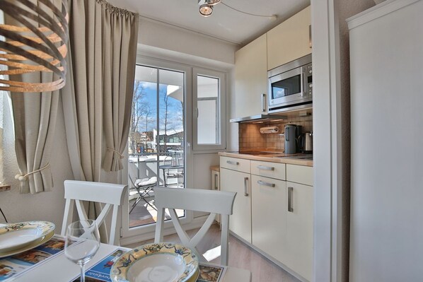 A compact kitchen with a microwave, stove, and cabinets. There's a dining area with a table, chairs, and a glass.