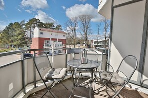 A balcony with two chairs and a table, overlooking a parking area and buildings.