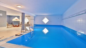 Piscina interior com chão azul, escada e área de espreguiçadeiras.