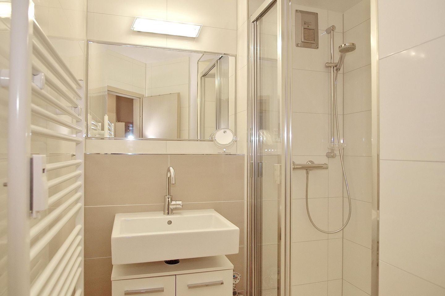 Un baño moderno con ducha de vidrio, lavamanos con espejo y perchero para toallas.