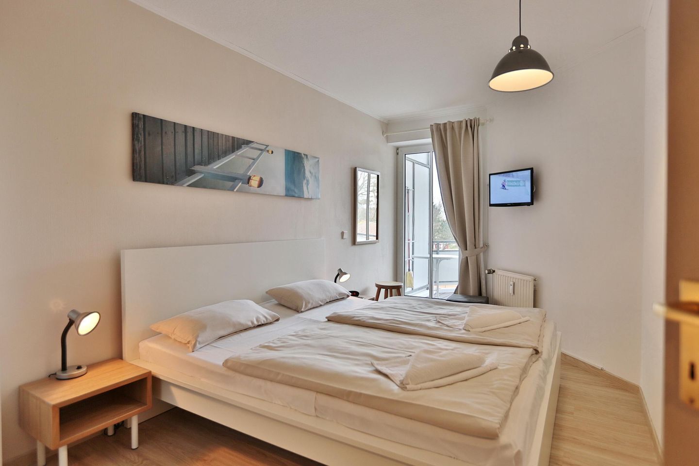 Quarto moderno com uma cama grande, uma mesa de cabeceira, um abajur, uma televisão e uma janela com cortinas.