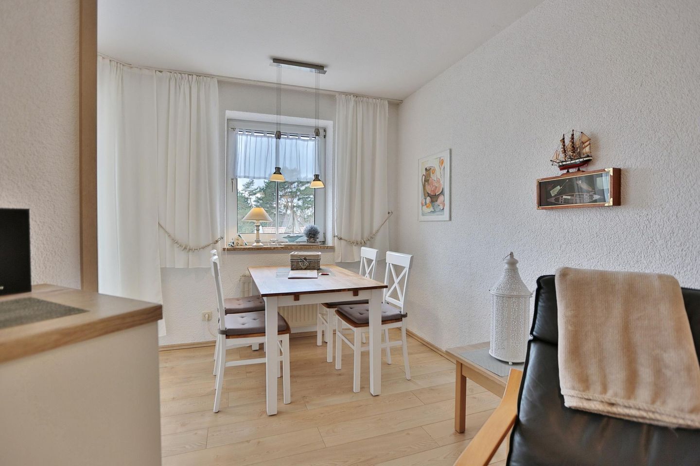 A modern living room with a black leather sofa, a wooden coffee table, and a dining area with a white table and chairs.
