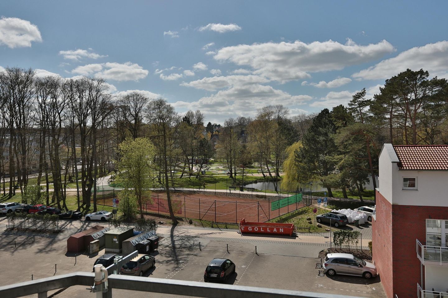 Un’area di parcheggio con diverse auto, un campo da tennis e un edificio con la scritta 'GOLLAN' sullo sfondo.
