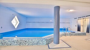 An indoor swimming pool with a tiled floor and walls, a central pillar, and a small seating area with a ladder.