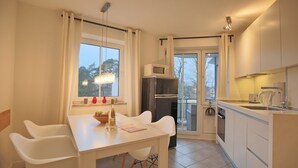 A modern kitchen with white cabinetry, a dining table with chairs, a refrigerator, a microwave, and a coffee maker.