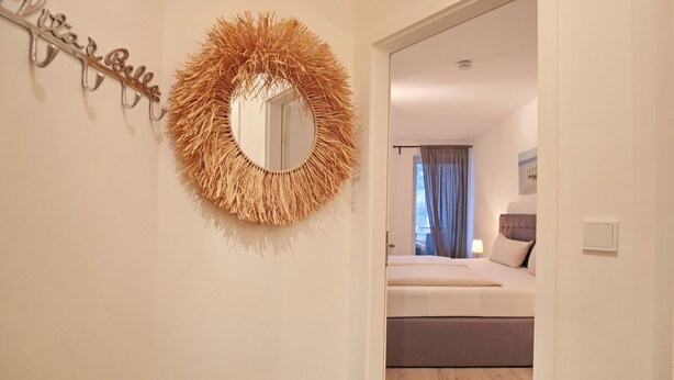 A bedroom with a bed, a bedside table, a mirror, and a wall-mounted light fixture.
