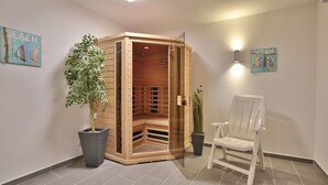 A sauna room with a wooden bench, a chair, and two potted plants.