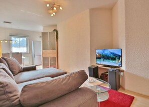 Una sala de estar moderna con un sofá, una mesa de centro de vidrio, un televisor de pantalla plana y una alfombra roja.