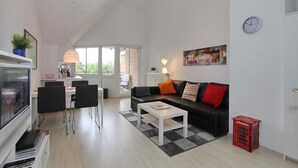A modern living room with a black sofa, white coffee table, and a dining area with chairs and a table.