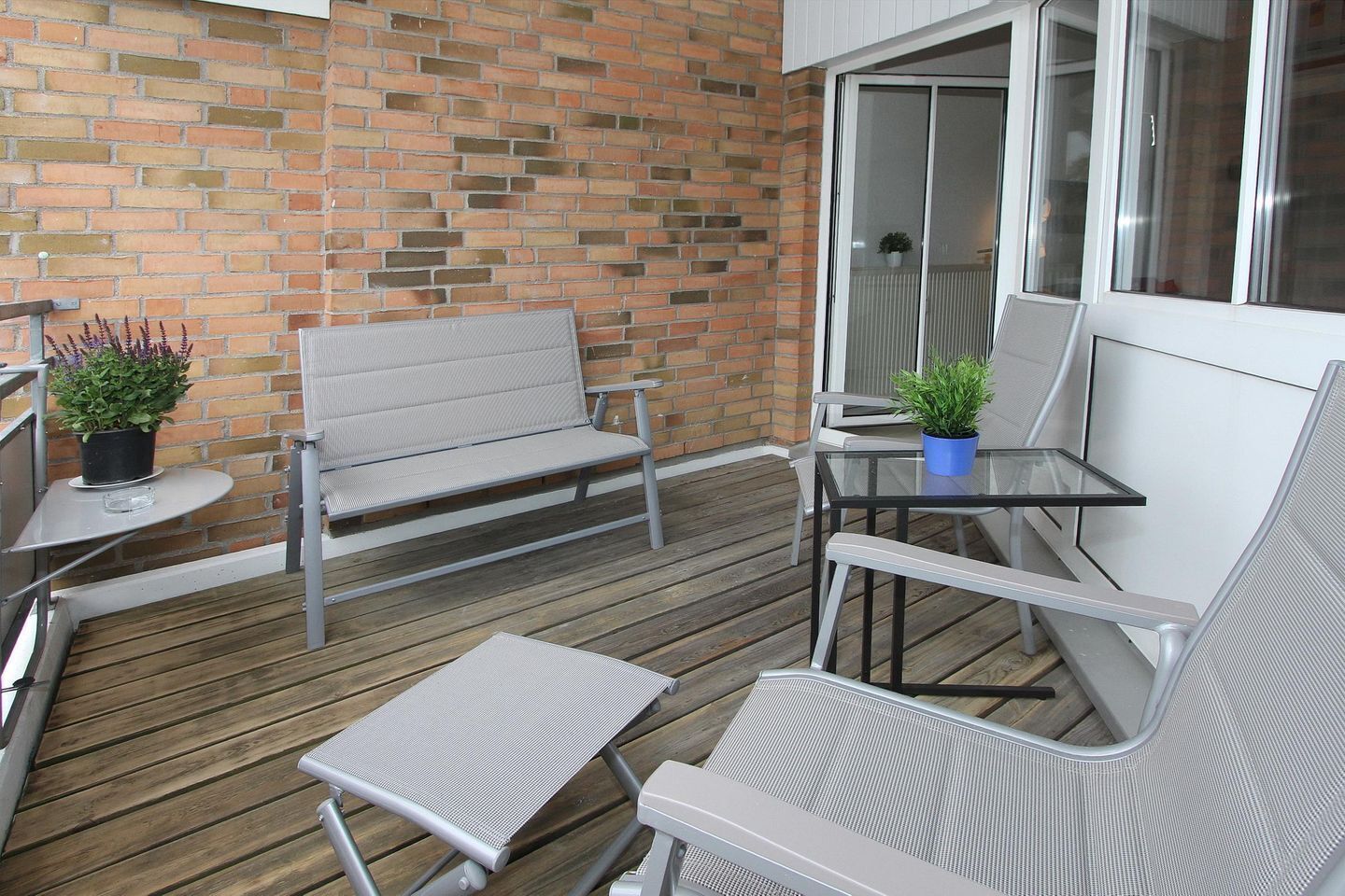 Eine Terrasse mit einer Ziegelmauer, einem Glastisch und zwei Stühlen.